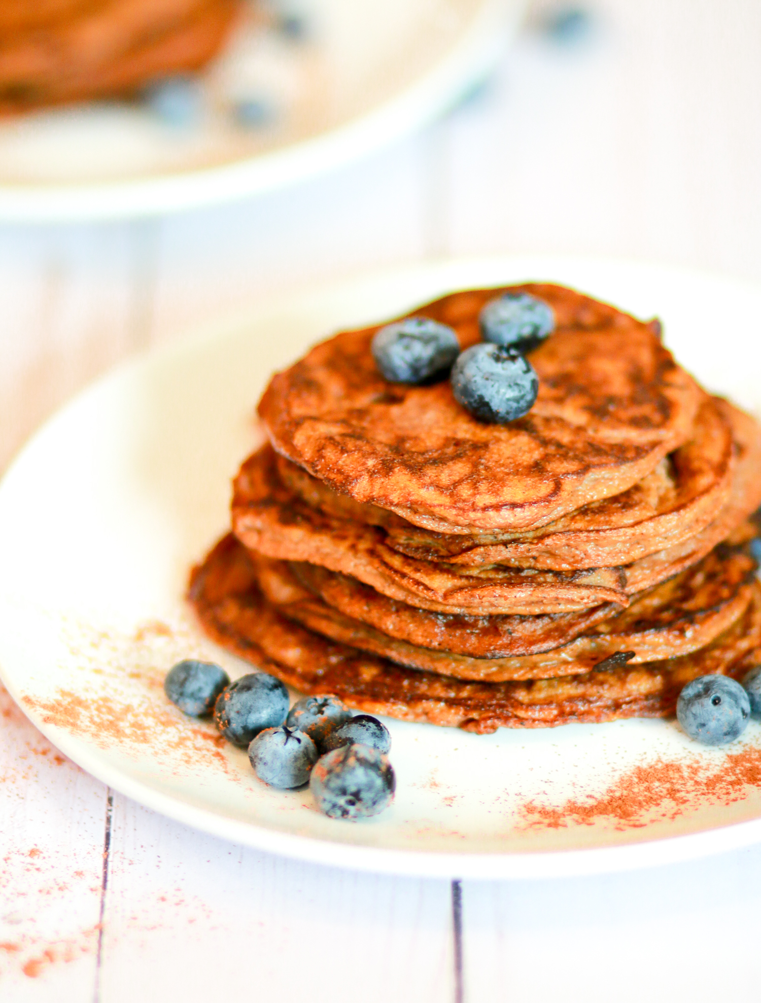 Plate of paleo pumpkin pancakes on a plate surrounded with cinnamon and blueberries